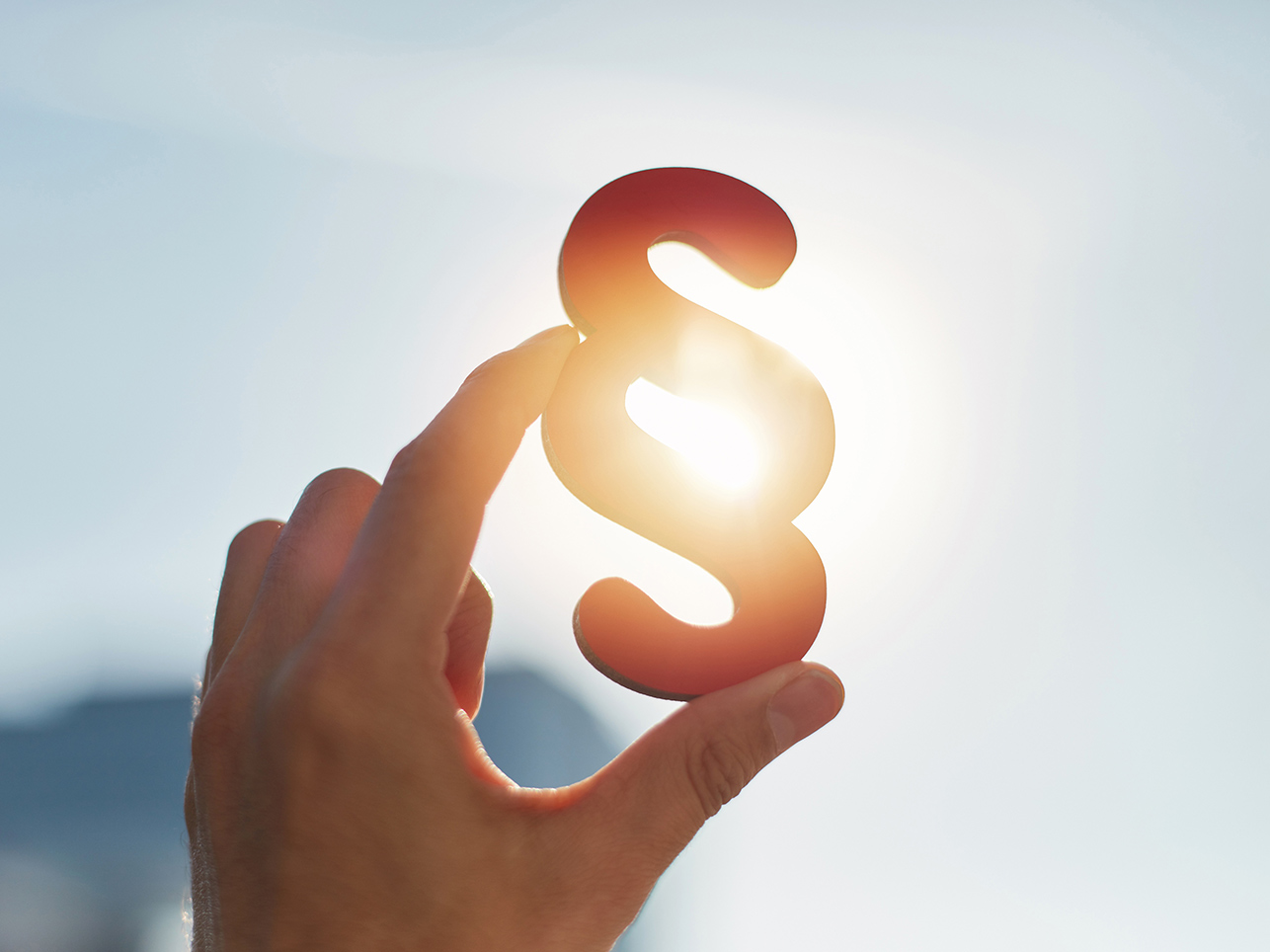 Paragrafenzeichen wird von einer Hand in die Luft gehalten