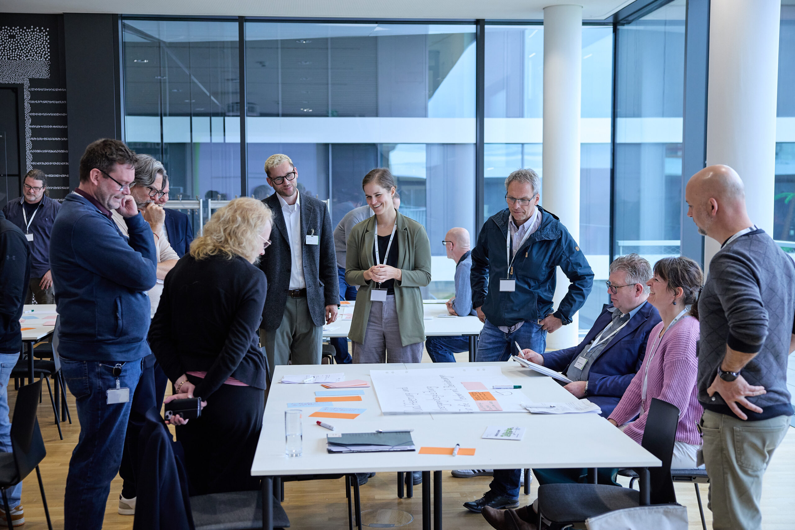Diskussionsszene beim Mitglieder:Dialog 2026 der BAG WfbM. Die Teilnehmenden stehen um einen Tisch und diskutieren.