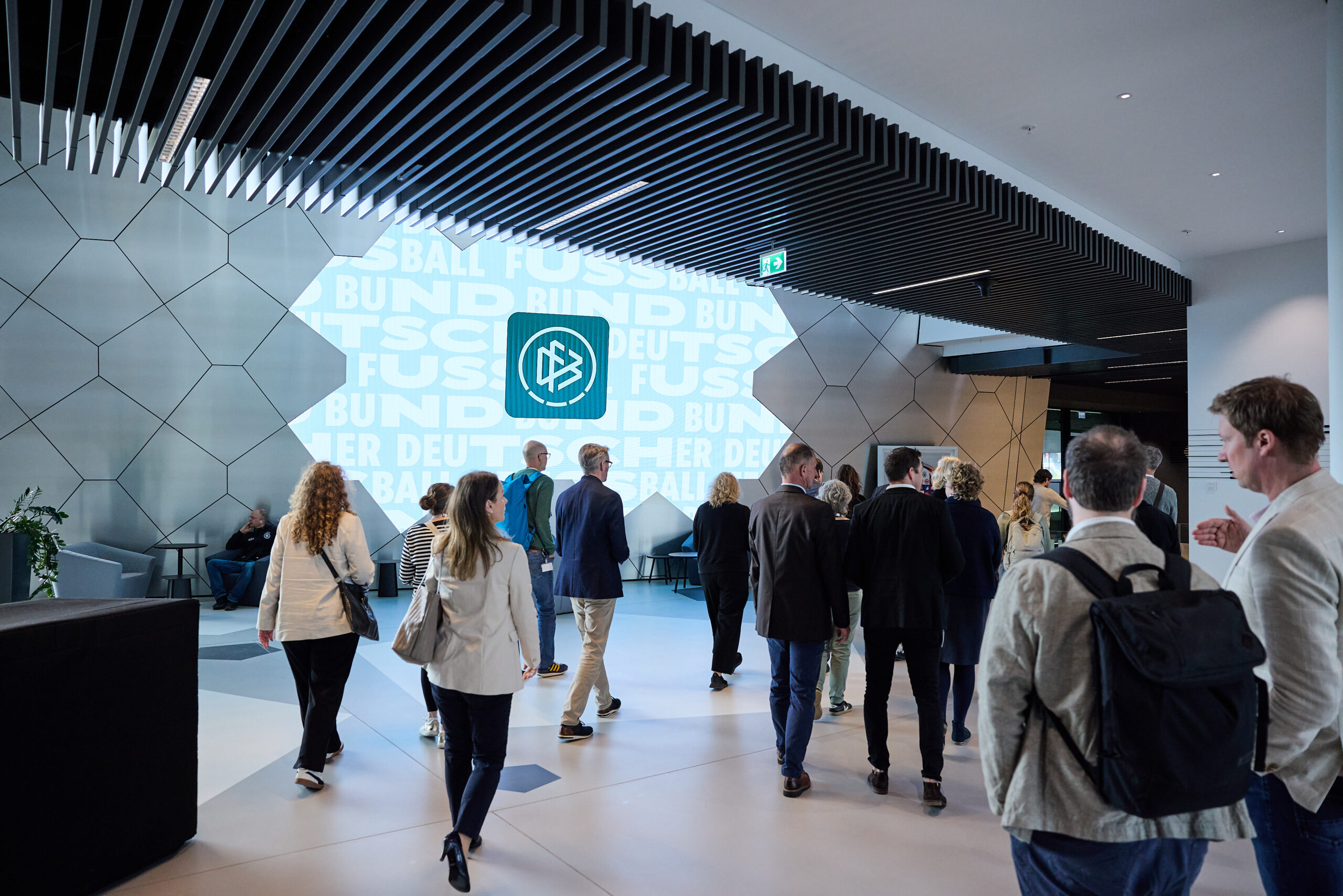 Die Teilnehmenden des Mitglieder:Dialogs 2026 der bAG WfbM bewegen sich durch das Gebäude des DFB-Campus Frankfurt. Im Hintergrund sieht man das Logo des DFB.