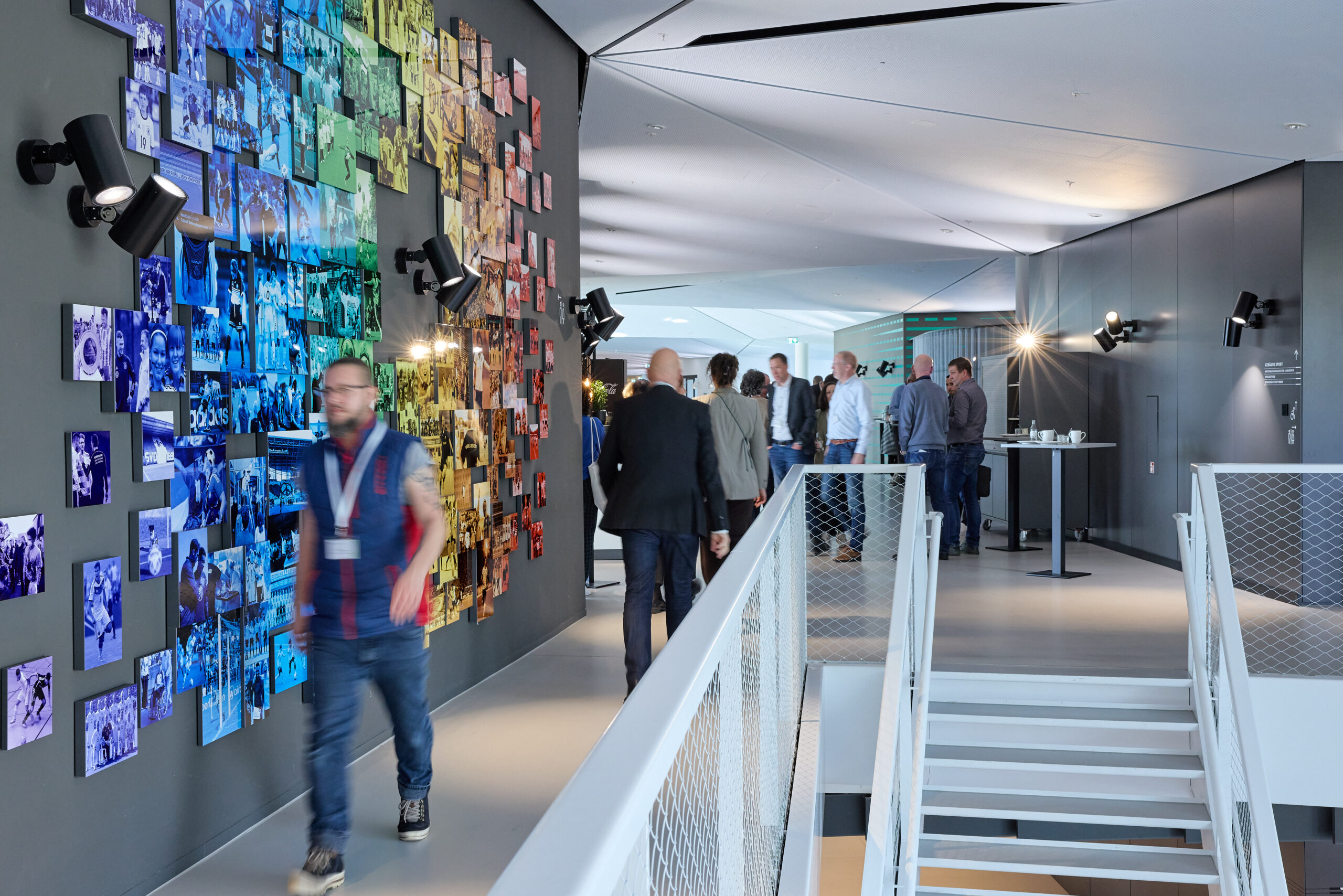 Die Teilnehmenden des Mitglieder:Dialogs 2026 der BAG WfbM bewegen sich durch das Gebäude des DFB-Campus in Frankfurt. Im Hintergrund sieht man eine regenbogenfarbene Fotowand.