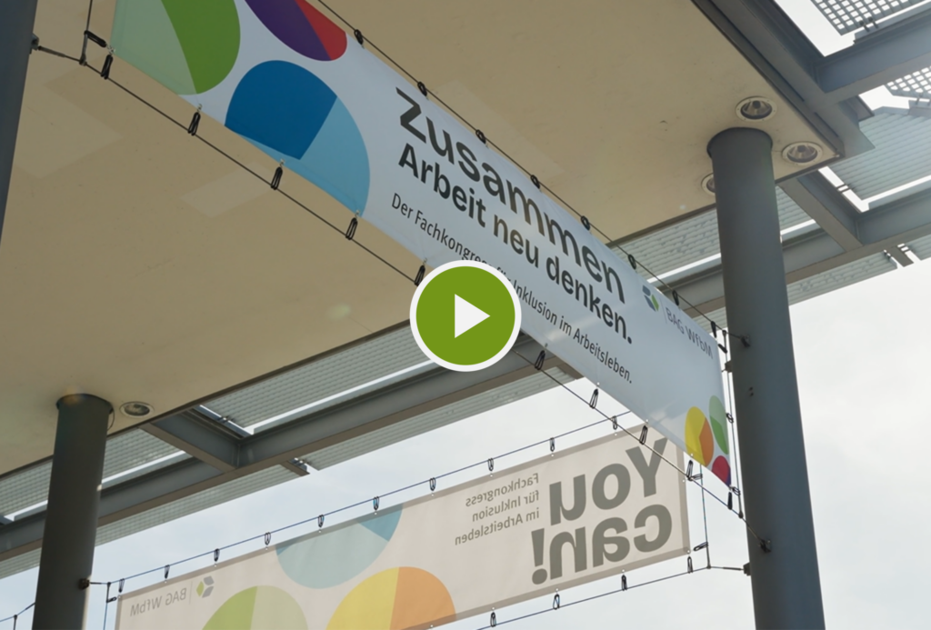 Titelbild des Kurzfilms zum Rückblick auf You can! 2026. Das Foto zeigt zwei große Werbebanner für die Veranstaltung, die an Säulen unter einem großen Vordach hängen. In der Mitte des Fotos ist ein weißer Play-Button in einem grünen Kreis platziert.