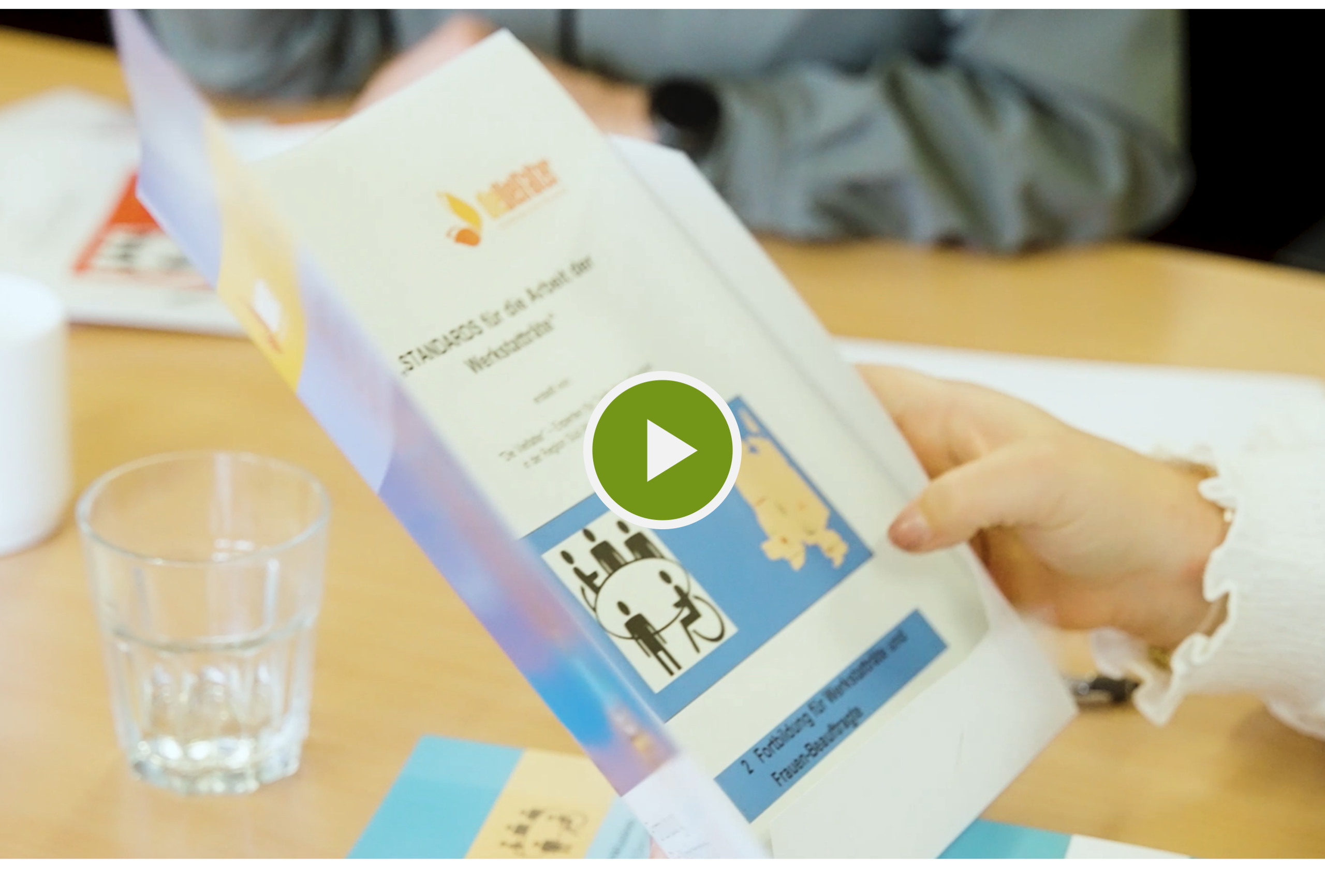 Das Foto zeigt einen Ausschnitt aus einer Sitzung. Eine Person hält eine aufgeklappte Handreichung in den Händen. Die Handreichung enthält Text und verschiedene Zeichnungen.