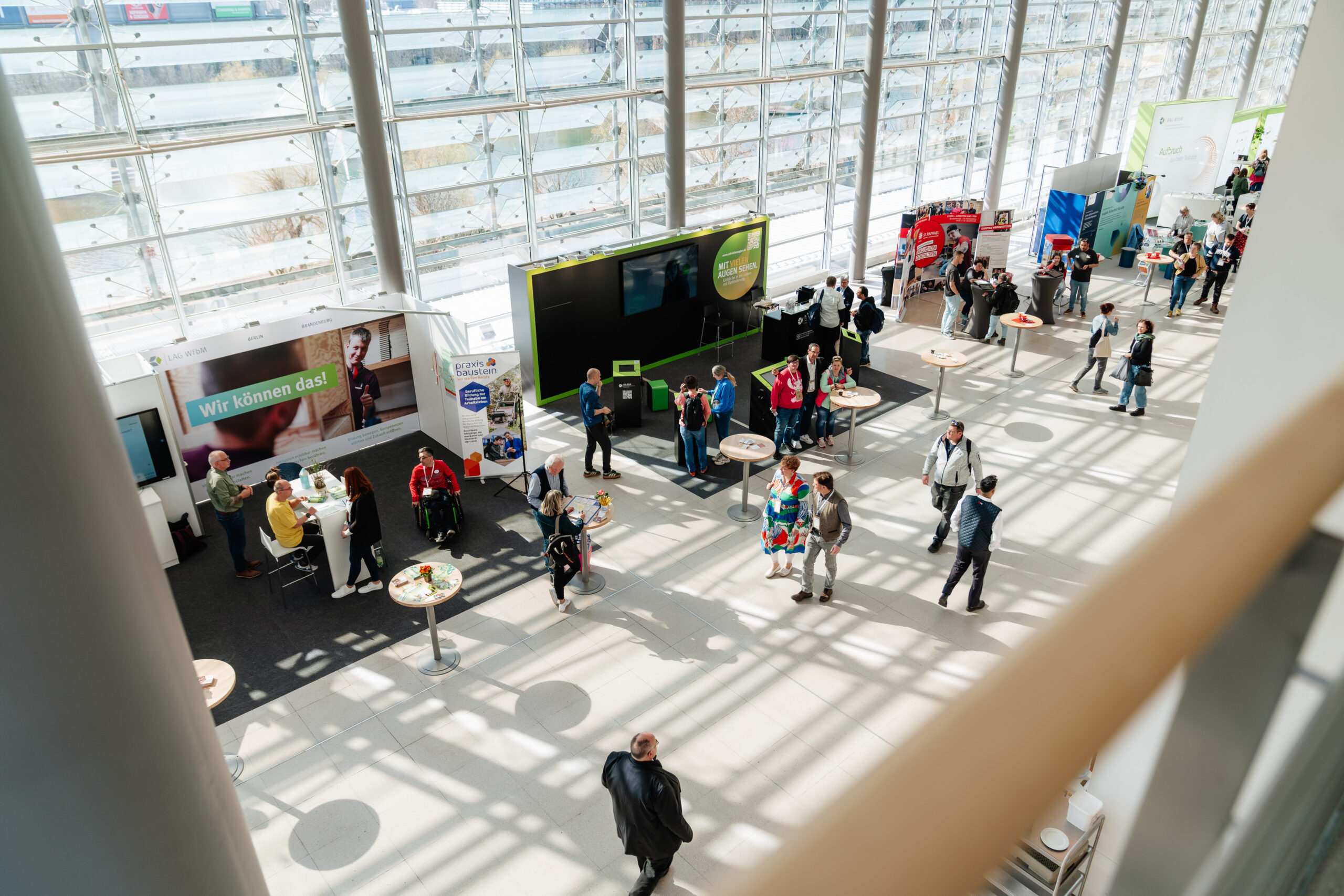 Das Foto zeigt mehrere Stände im Rahmen der Ausstellung beo You can! 2026. Sie befinden sich in einem luftdurchfluteten Atrium. Menschen laufen umher oder stehen an den Ständen und unterhalten sich. Das Foto ist aus einem Stockwerk über der Ausstellung aufgenommen, sodass alles aus der Vogelperspektive sichtbar ist.